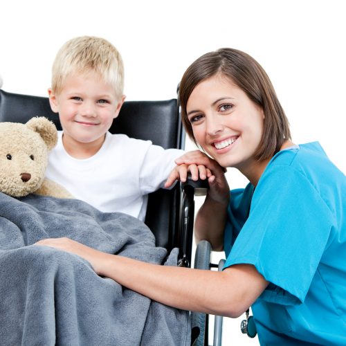 Nice female doctor carrying adorable little boy with his teddy bear in the wheelchair at the hospital